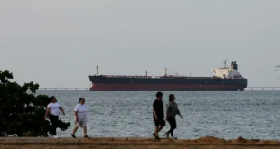 People pass by as an oil tanker is seen on Lake Maracaibo, loaded with petroleum, waiting to depart for refineries in the United States, in Maracaibo, Venezuela, on May 11, 2026. [Jose Isaac Bula – Anadolu Agency ]
