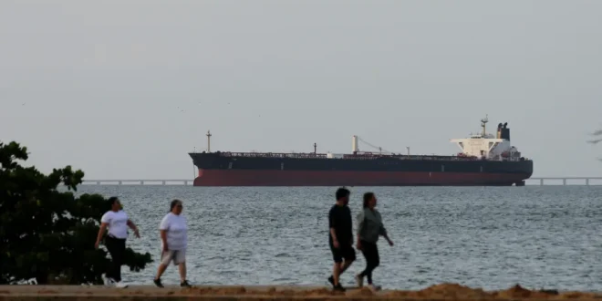 People pass by as an oil tanker is seen on Lake Maracaibo, loaded with petroleum, waiting to depart for refineries in the United States, in Maracaibo, Venezuela, on May 11, 2026. [Jose Isaac Bula – Anadolu Agency ]